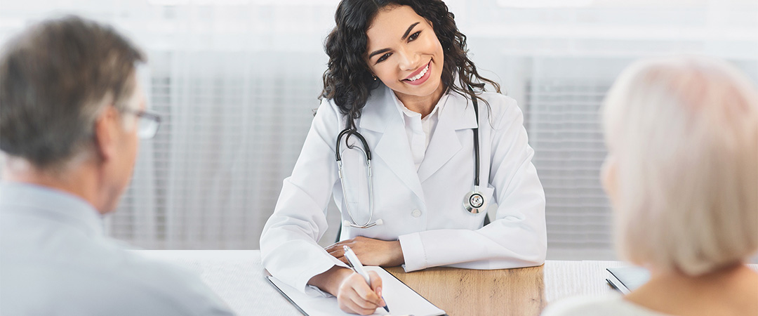 Doctor with a stethoscope draped around her neck taking notes while speaking to a couple