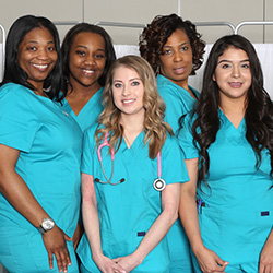 Five nurses wearing teal scrubs in front of a privacy curtain