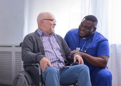 Male nurse kneeling down to speak with a resident in a wheelchair