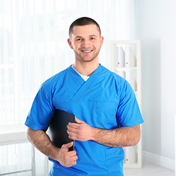 Male nurse wearing blue scrubs and smiling while standing in a hallway